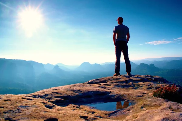 Solo uomo in berretto rosso sulla vetta di picco tagliente nel parco imperi rocciosi e guardando sopra la nebbiosa e nebbiosa valle del mattino al sole. Momento bellissimo — Foto Stock