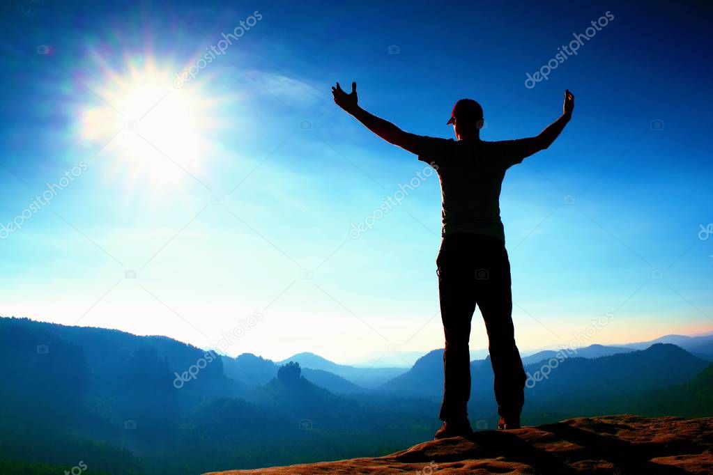 Happy man gesture in red cap of triumph with hands in the air. Funny hiker on the peak of sandstone rock in Saxony Switzerland park