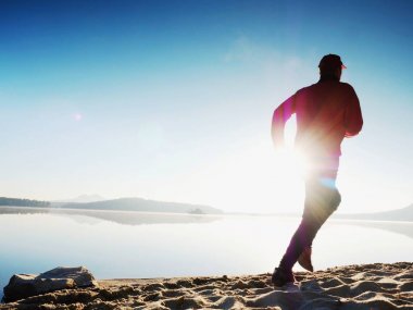 Egzersiz ve göl kumsalda güneş doğarken germe etkin adam silüeti.