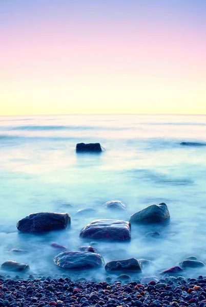 Romantic morning at sea. Big boulders sticking out from smooth wavy sea. Long exposure — Stock Photo, Image