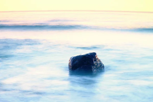 Romantic atmosphere in peaceful morning at sea. Big boulders sticking out from smooth wavy sea. Pink horizon — Stock Photo, Image