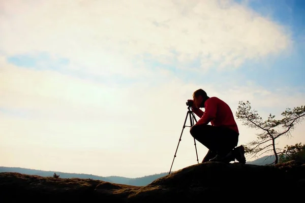 Fotógrafo amador tira fotos com câmera de espelho no pico da rocha. Paisagem nebulosa sonhadora, primavera laranja rosa nebuloso nascer do sol — Fotografia de Stock