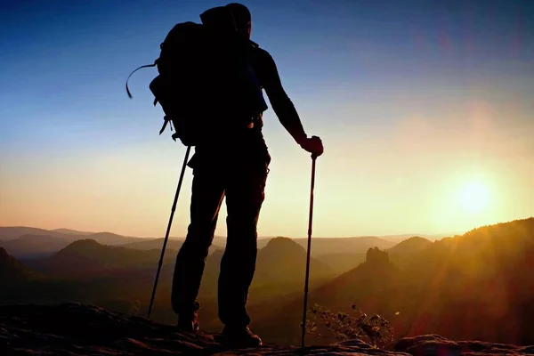 Tall backpacker with poles in hand. Sunny hike day in rocky mountains. Hiker with big backpack stand on rocky view point above misty valley. — Stock Photo, Image