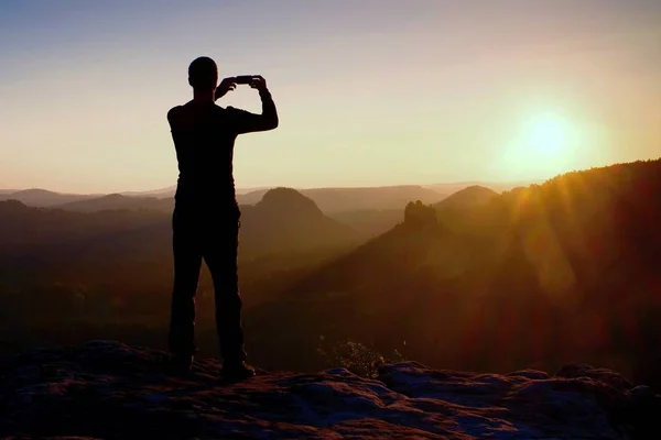 L'escursionista sta scattando foto con lo smartphone sulla cima della montagna all'alba . — Foto Stock