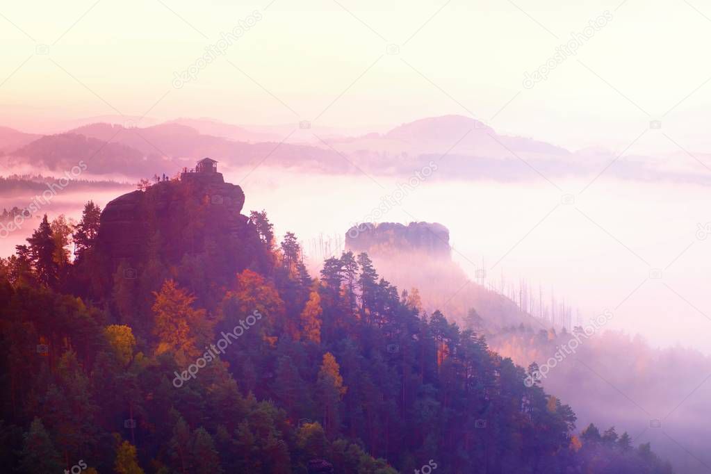 Cold misty daybreak in a fall valley of Bohemian Switzerland park. Hill with hut on the peak increased from magical darkness. 