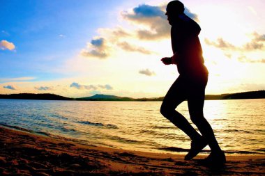 Siluet spor etkin adam çalıştıran ve canlı renkli batımında sahilde egzersiz.