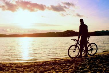 Genç adam bisikletçi siluet mavi gökyüzü ve sunset beach yukarıda. Sezon sonunda göl, motorcu.