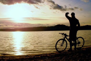 Genç adam bisikletçi siluet mavi gökyüzü ve sunset beach yukarıda. Sezon sonunda göl, motorcu.