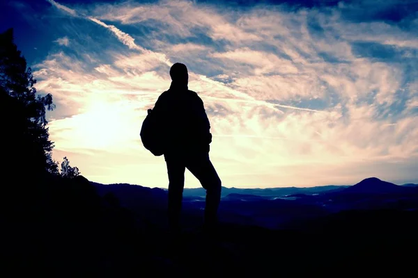 Turista se sportovní batoh stojí na skalní vyhlídka a dívají se do hlubokých mlhavé údolí níže. Slunečné jarní svítání v rocky mountains. — Stock fotografie