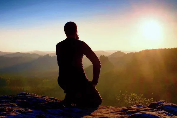 Caminante deportivo en ropa deportiva negro sentarse en la cima de la montaña y tomar un descanso. Vigilancia turística hasta el valle brumoso de la mañana . — Foto de Stock