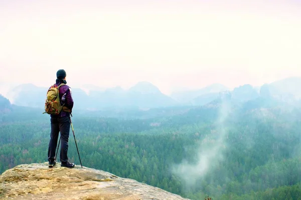 Hiker with backpack and poles on cliff rock  watching over the misty and foggy spring valley to Horizon. — Stock Photo, Image