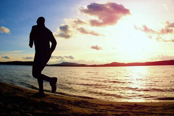 Silhouet van sport actieve man uitgevoerd en uitoefening op strand bij levendige kleurrijke zonsondergang. — Stockfoto