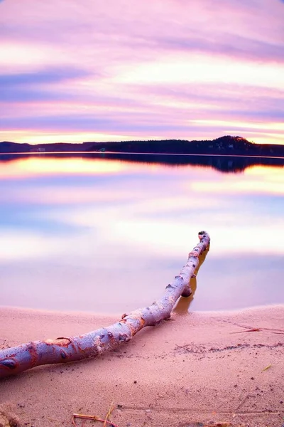 Lange Belichtung des Seeufers mit abgestorbenem Baumstamm, der nach Sonnenuntergang ins Wasser gefallen ist. — Stockfoto