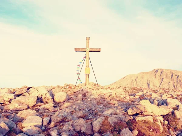 Praying flags fluttering  in the wind on the summit cross. Wooden crucifix on top of Alpine mountain — Stock Photo, Image