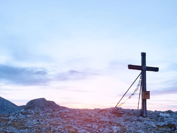 Praying flags fluttering  in the wind on the summit cross. Wooden crucifix on top of Alpine mountain — Stock Photo, Image