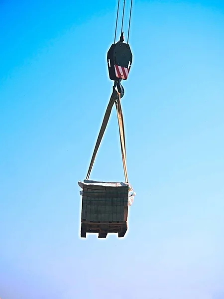 Grúa gancho con ladrillos blancos apilados en una plataforma de madera, cielo azul claro en el fondo — Foto de Stock