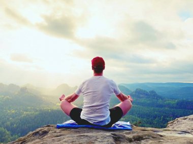 Yalnız adam pratik Yoga poz kayalık tepe üzerinde oturuyor. Adam puslu sabah içinde meditasyon yapmak 