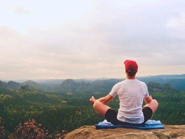 Yalnız adam pratik Yoga poz kayalık tepe üzerinde oturuyor. Adam puslu sabah içinde meditasyon yapmak 