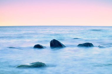Denizde romantik sabah. Yumuşak su seviyesinden yapışkanlık dışarı büyük kayalar. İlk sıcak güneş ışınları ile pembe horozon.