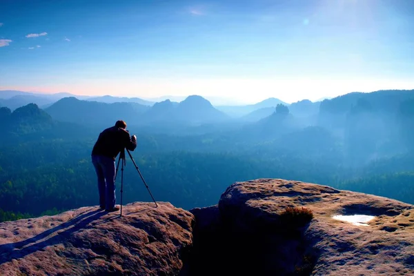 Professional on cliff. Nature photographer takes photos with mirror camera on peak of rock. Dreamy blue fogy landscape, — Stock Photo, Image