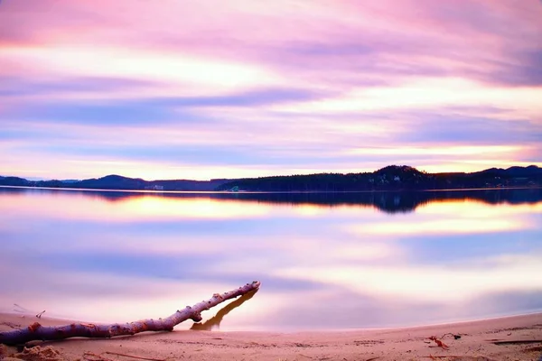 Lange Belichtung des Seeufers mit abgestorbenem Baumstamm, der nach Sonnenuntergang ins Wasser gefallen ist. — Stockfoto