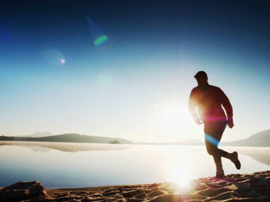  egzersiz ve göl kumsalda güneş doğarken uzanan bir adam. Sağlıklı bir yaşam tarzı. Yalnız genç fitness adam egzersiz sabah kumsalda