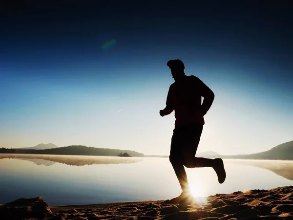 Hombre haciendo ejercicio y estirándose en la playa del lago al amanecer. Estilo de vida saludable. Solo joven fitness hombre ejercicio en la playa de la mañana — Foto de Stock