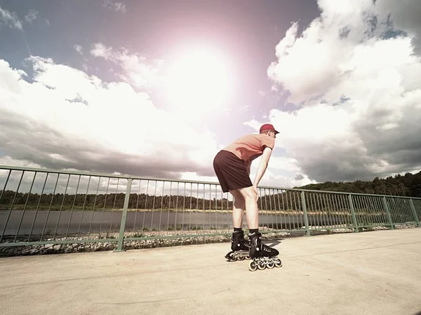 Roller skater w akcji. Mężczyzna jazdy inline Łyżwy przejażdżkę wzdłuż promenady poręczy, niebo w tle — Zdjęcie stockowe