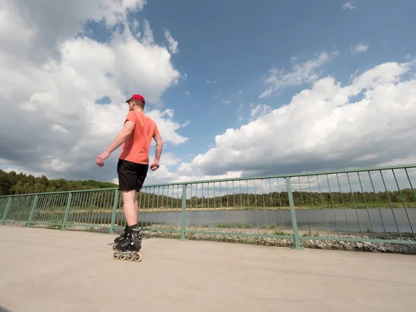 Kolečkové bruslaře v akci. Muž jízda na inline bruslích jízda podél promenády zábradlí, obloha pozadí — Stock fotografie