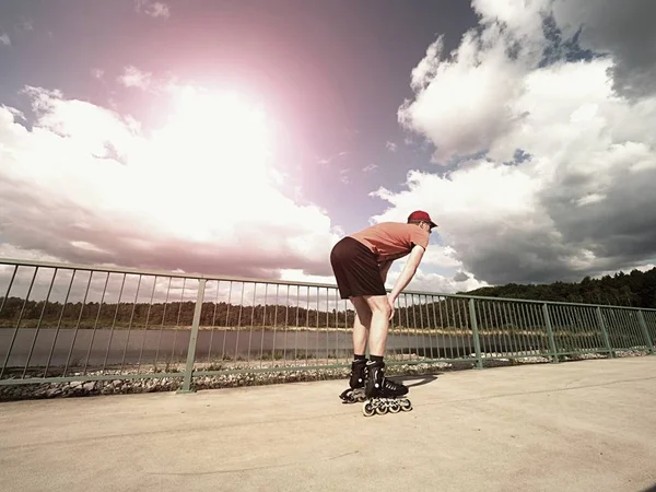 Middle age man in red t-shirt  with inline skates ride in summer park, popular outdoor skating.