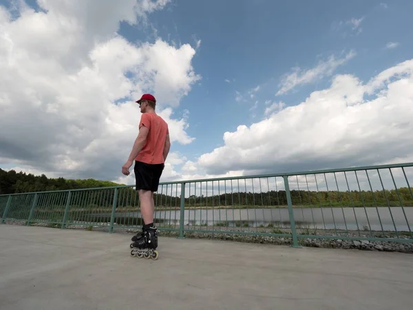 Roller skater w akcji. Mężczyzna jazdy inline Łyżwy przejażdżkę wzdłuż promenady poręczy, niebo w tle — Zdjęcie stockowe