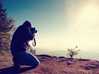 Adamlara vadiye fotoğrafçı arayın. Adam uçurumun üzerinde diz çökmüş ve fotoğraf çeker.