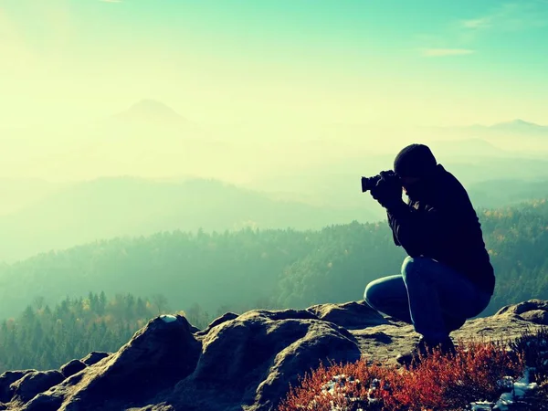 Photographer down on knees takes photos with mirror camera on peak of rock — Stock Photo, Image