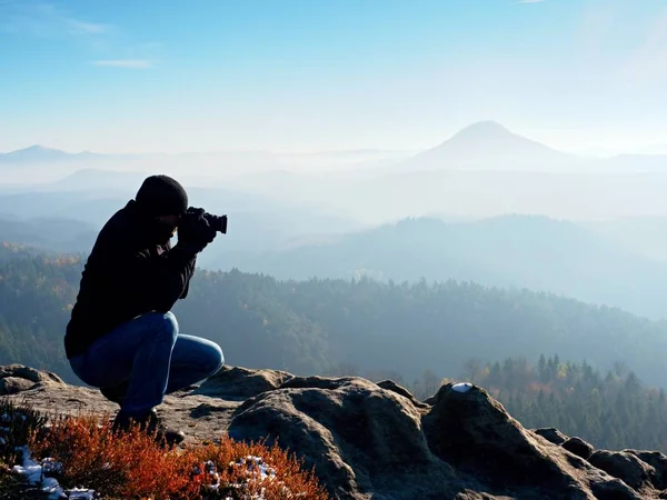 O fotógrafo olha para o vale nebuloso. Homem está ajoelhado em penhasco e tira fotos . — Fotografia de Stock