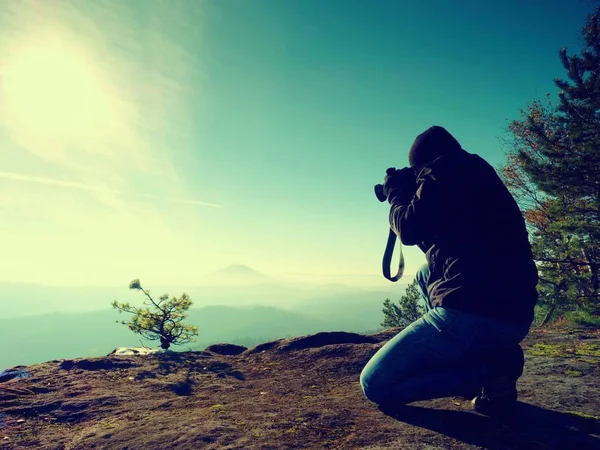 Il fotografo guarda giù nella nebbiosa valle. L'uomo si inginocchia sulla scogliera e scatta foto . — Foto Stock