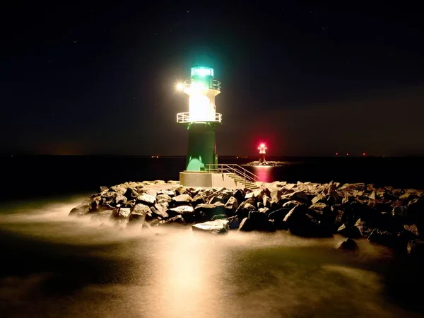 Grüner Leuchtturm leuchtet am Ende der steinigen Seebrücke in dunkler Nacht — Stockfoto