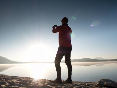 Onun arkasında da Denizi selfie fotoğraf çekmek için cep telefonu kullanarak deniz kenarında yalnız adam