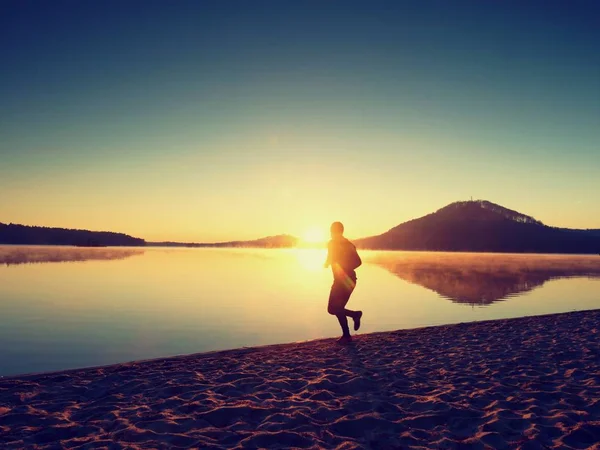Homme courant sur la plage sur fond d'un beau coucher de soleil. Sable du lac de montagne — Photo