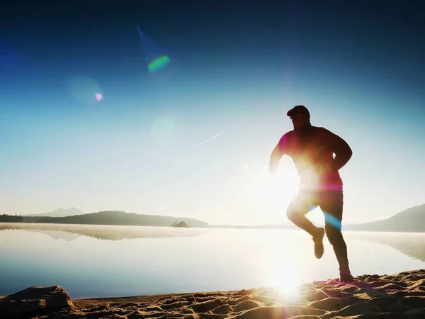 Hombre corriendo en la playa contra el telón de fondo de una hermosa puesta de sol. Arena de lago de montaña —  Fotos de Stock