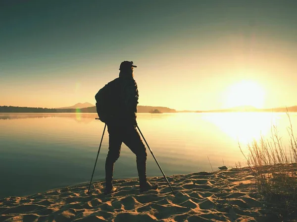 Older man tourist standing close to water on empty beautiful beach. The hot sun rising up