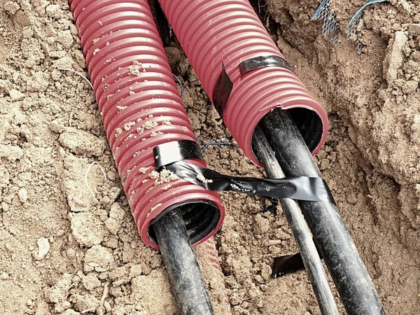 Excavation of trench with black cables in protective HDPE tube. Lines of metallic and fiber optic wires. — Stock Image Excavation of trench with black cables in protective HDPE tube. Lines of metallic and fiber optic wires. Royalty Free Stock Photos