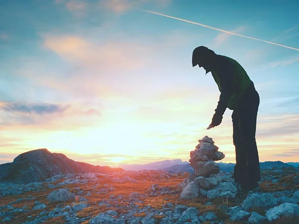 Turysta człowiek buduje pebbles ostrosłupa. Kamienie na szczycie góry Alpy. Horyzontem brzask — Zdjęcie stockowe