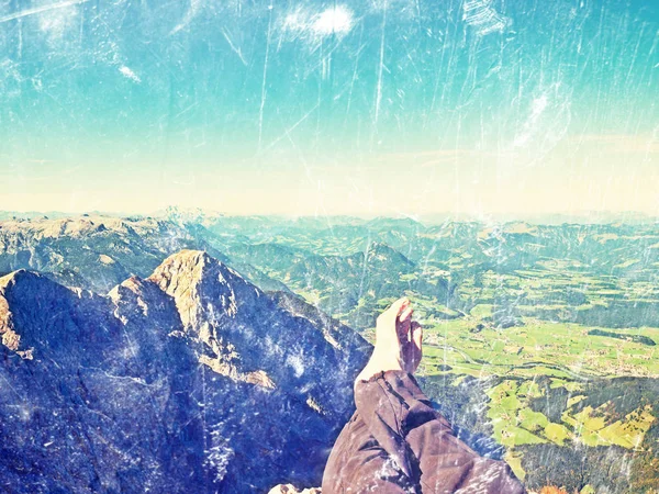 Film grain effect.  The crossed legs take a  rest on tiring mountain trail. Sweaty male legs relaxing on peak of mountain