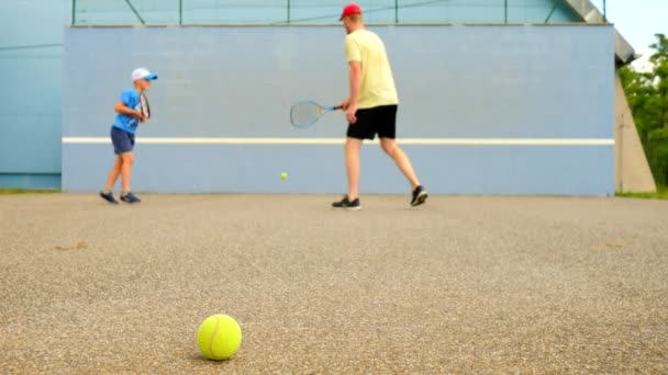 Pai e filho praticam ténis na parede de treino. Jogadores de passatempo com raquete e bola jogando na quadra — Vídeo de Stock