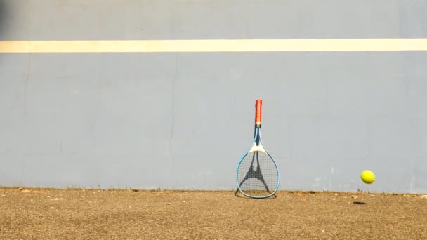 Hüpfender Tennisball gegen Wand. Tennisball springt auf den Platz, sehr alter Aluminnum-Tennisschläger lehnt an der Wand. — Stockvideo