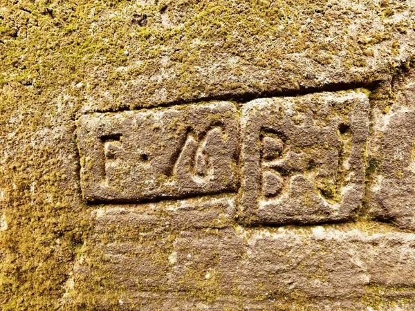 Oyma yazıtlı eski gri taş duvar. Kumtaşı duvar oyma harf ve sayı ile — Stok fotoğraf