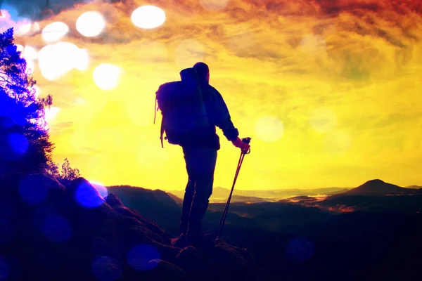 Пленка. Турист с тяжелым рюкзаком и палками в руках стоит на скалистой смотровой площадке и наблюдает за глубокой туманной долиной. Солнечный весенний рассвет в скалистых горах . — стоковое фото