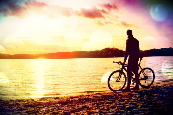 Grão de filme. Jovem ciclista silhueta no céu azul e pôr do sol de fundo na praia. Fim de estação no lago . — Fotografia de Stock