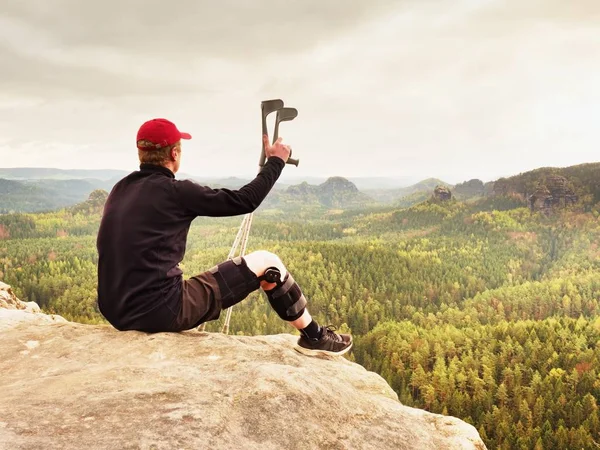 Tıp koltuk değneği ile yorgun yaralı turist. Kırık bacak diz küme ayracı özellikleri üzerinde dinlenme adamla kayalık Zirvesi maruz