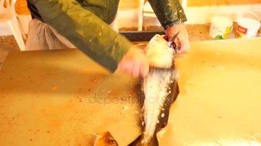 Cod, morina. Hızlı kaldırma-in ölçekler bir dosyalama masada bir tel fırça ile. Güçlü erkek görünümünü Deniz balığı ile çalışma eller. Kaldırılan ölçekler ve masanın üzerinde kan.
